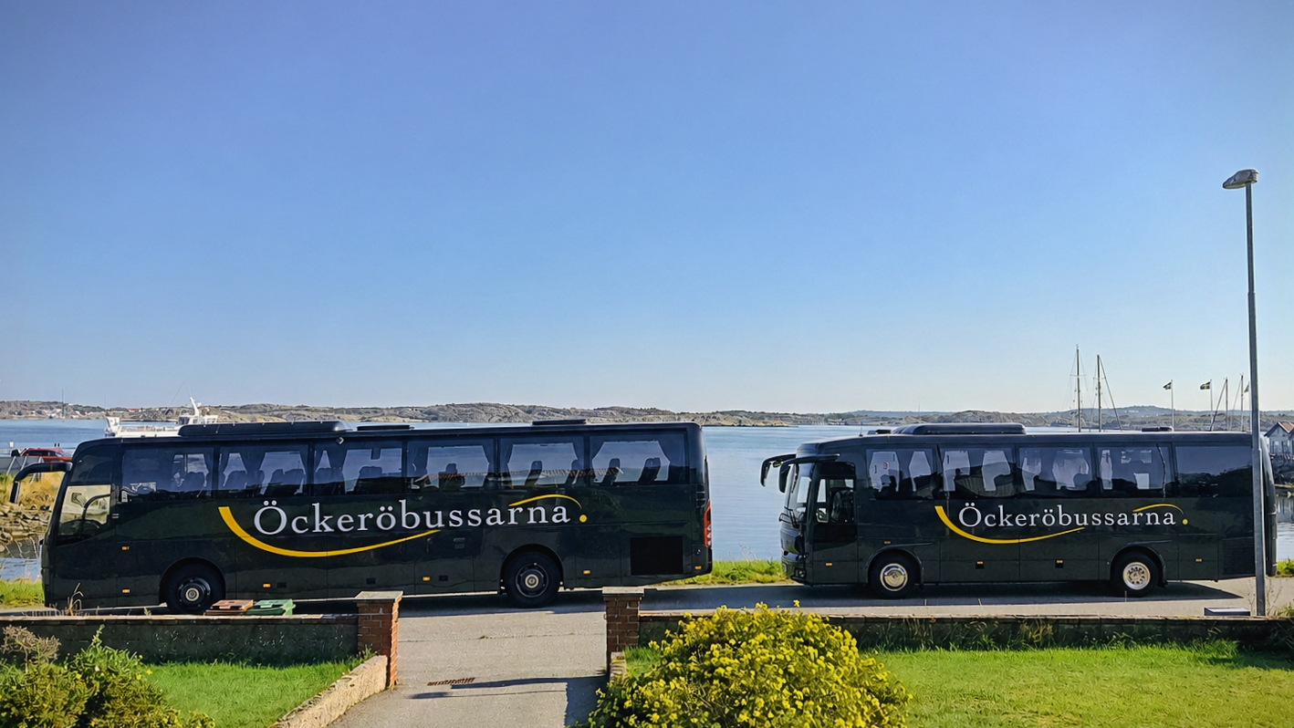 Två mörkgrå bussar från Öckeröbussarna vid en hamn med båtar och klippor